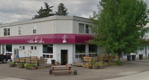 Corner view of a small white building with a red awning and patio seating surrounding it.